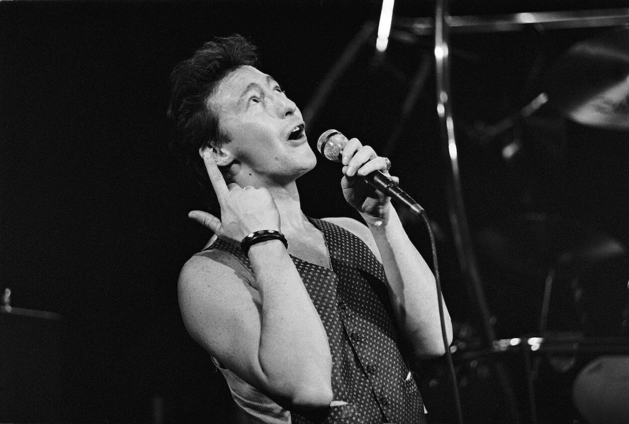 Julian Lennon singing into a microphone and pointing to the sky during a 1989 concert.