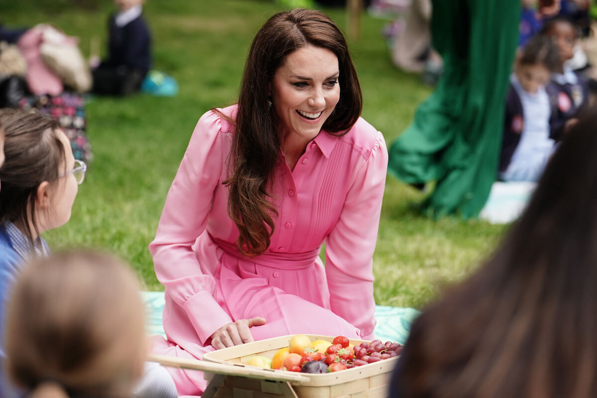 Kate Middleton, whose pink outfits are 'no coincidence' after pink gown at Jordan royal wedding, according to expert, sits on a blanket wearing a pink dress