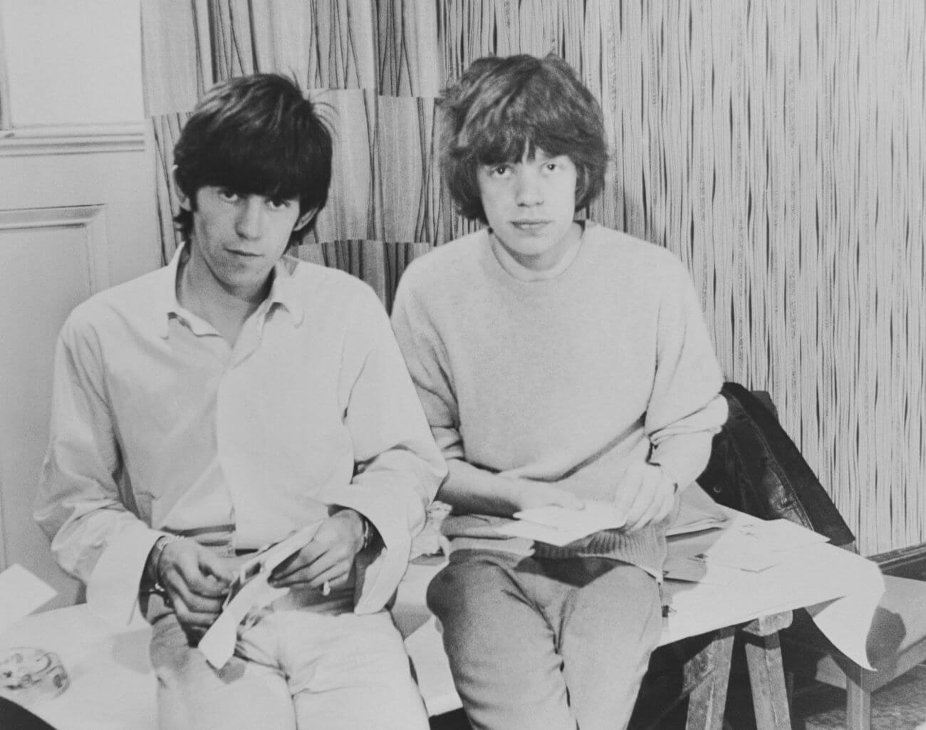 A black and white picture of Keith Richards and Mick Jagger sitting on a bench together.