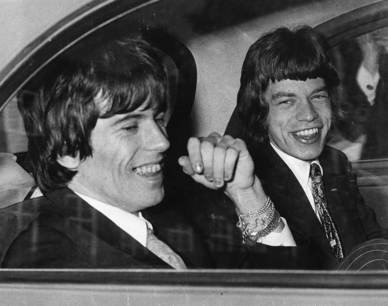 A black and white picture of Keith Richards and Mick Jagger sitting in the backseat of a car.