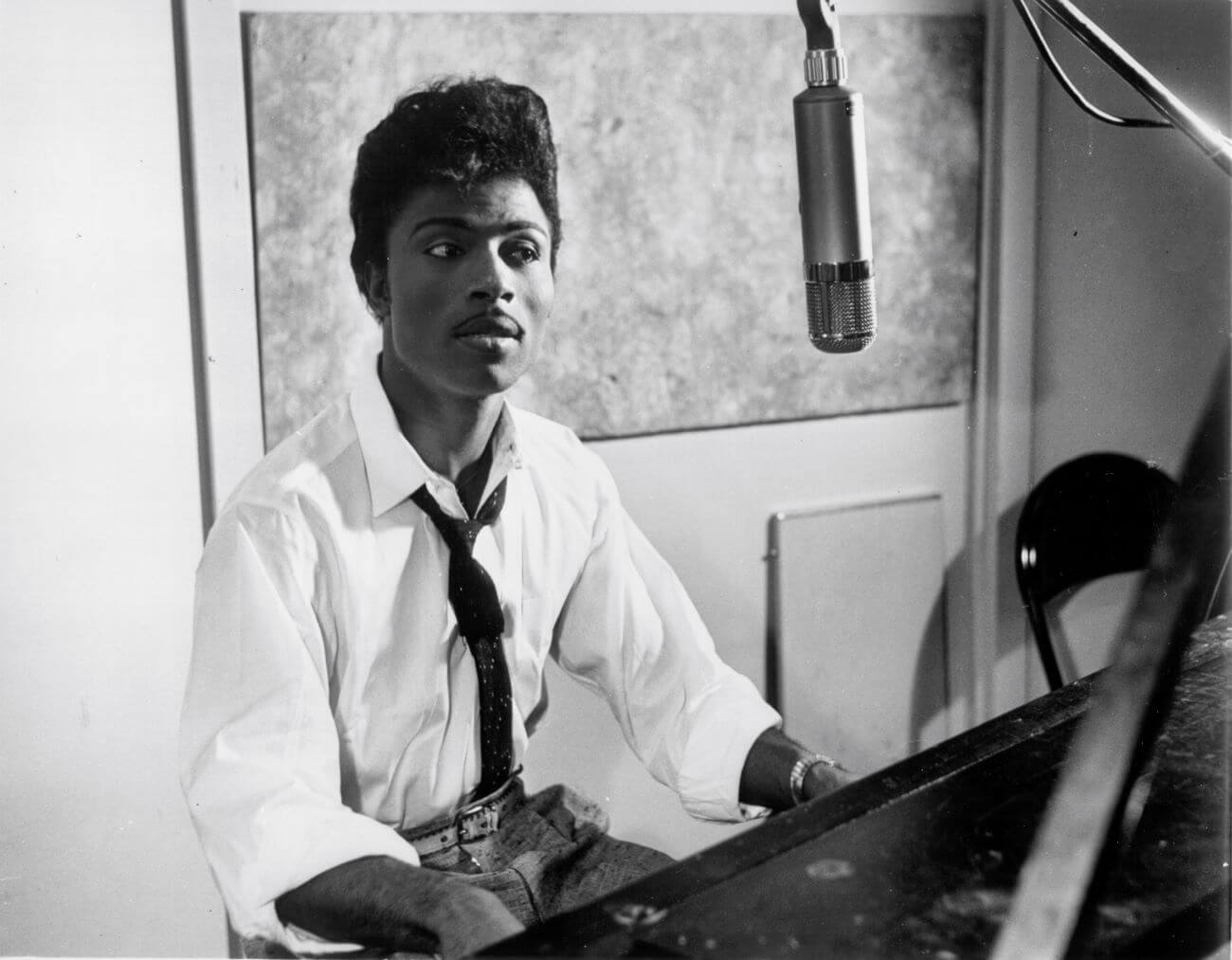 A black and white picture of Little Richard sitting at a piano with a microphone.