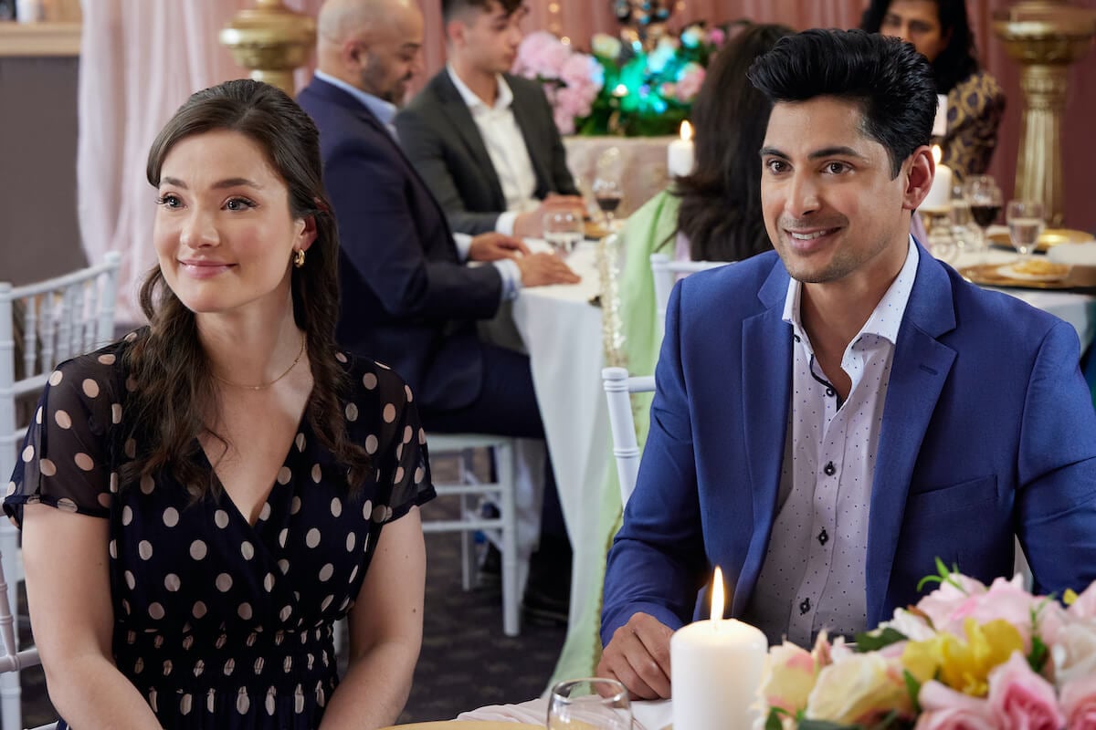 Eva Bourne and Rushi Kota sitting at a table in Hallmark's 'Make Me a Match'