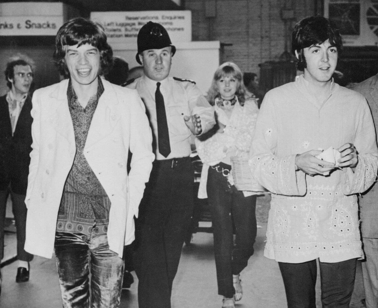 A black and white picture of Mick Jagger and Paul McCartney walking ahead of a police officer.