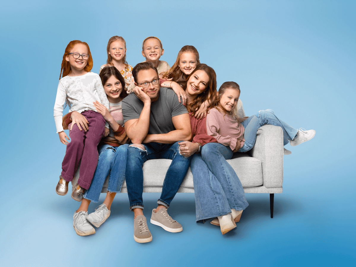 The Busby family on a blue background in a promotional image for 'OutDaughtered' on TLC