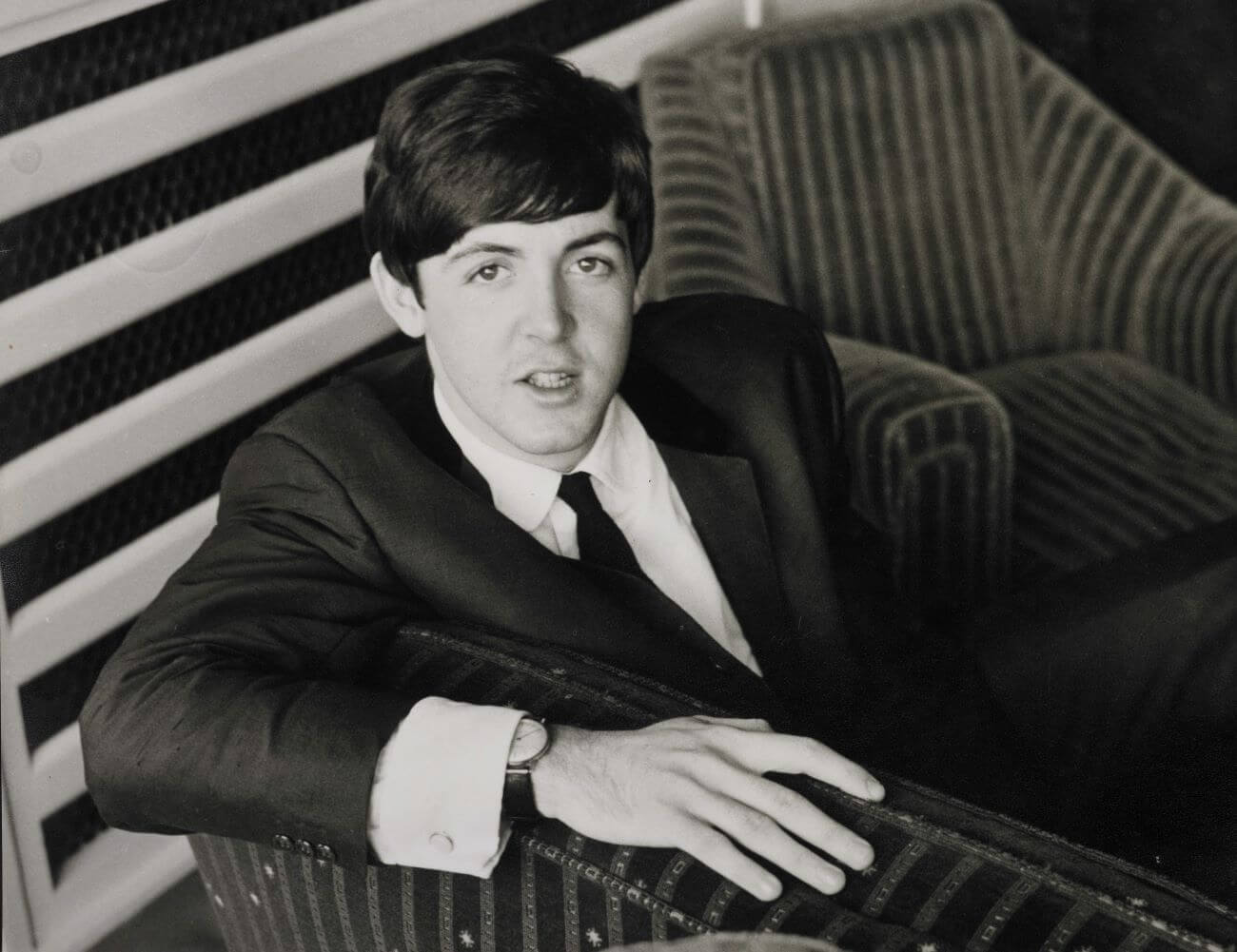 A black and white picture of Paul McCartney wearing a suit and sitting on a couch.