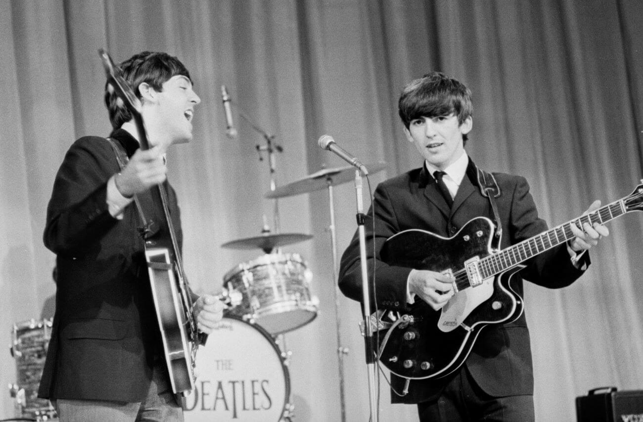 A black and white picture of Paul McCartney singing and playing guitar and George Harrison playing guitar.