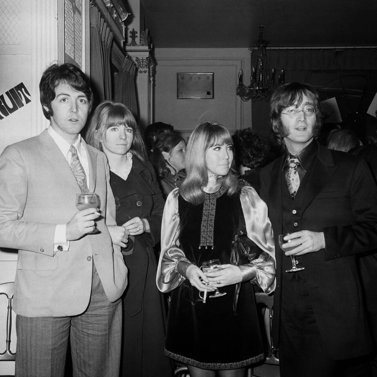 A black and white picture of Paul McCartney, Jane Asher, Cynthia Lennon, and John Lennon holding glasses and standing in a crowded room.