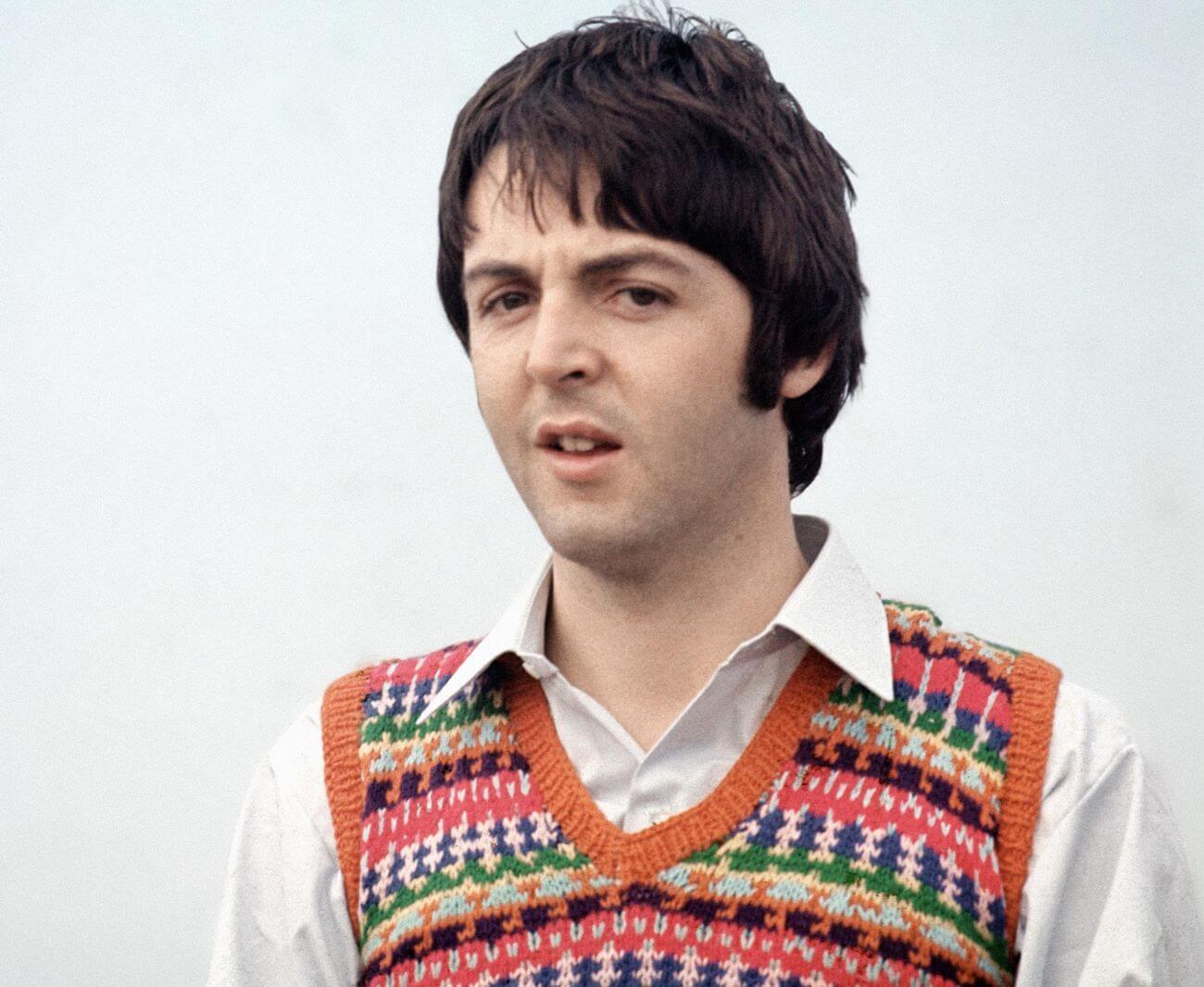 Paul McCartney wears a white collared shirt and a sweater vest.
