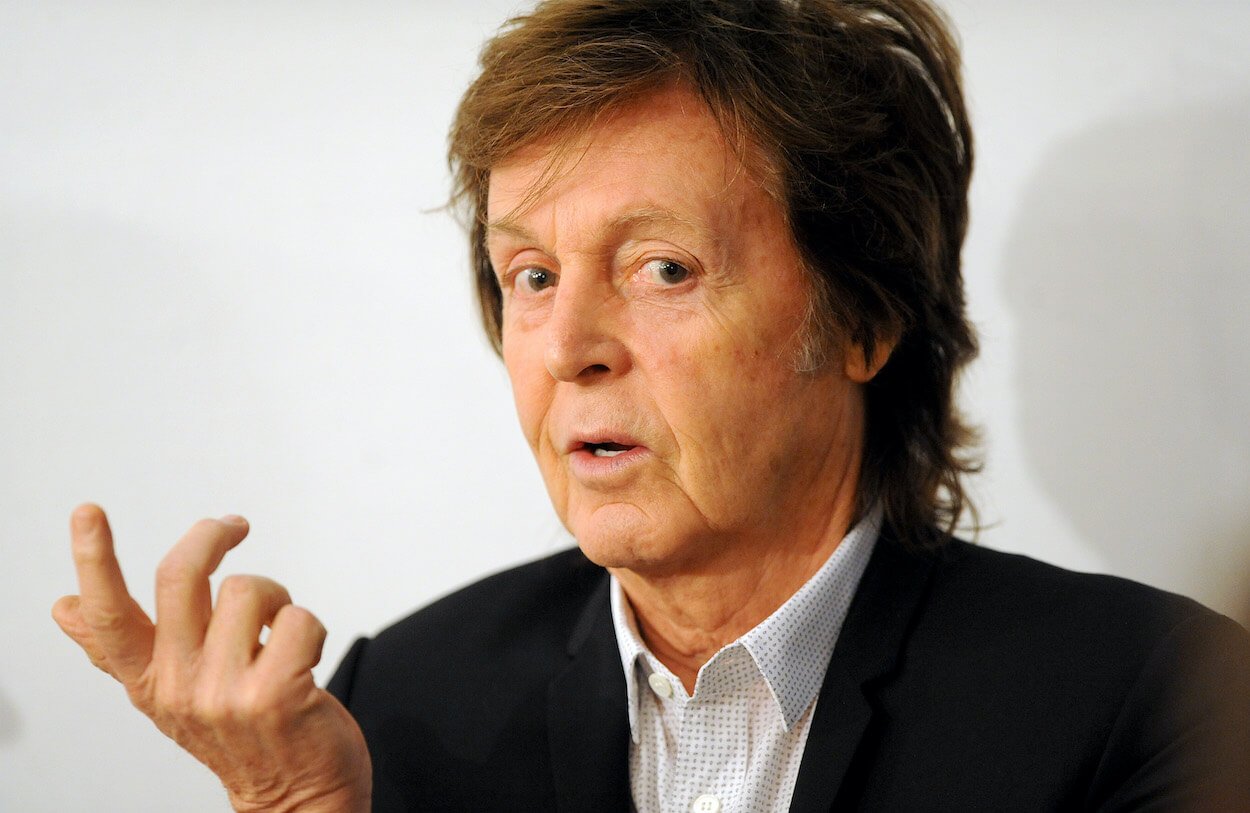 Paul McCartney elevating his right hand while wearing a dark suit during a 2014 event.