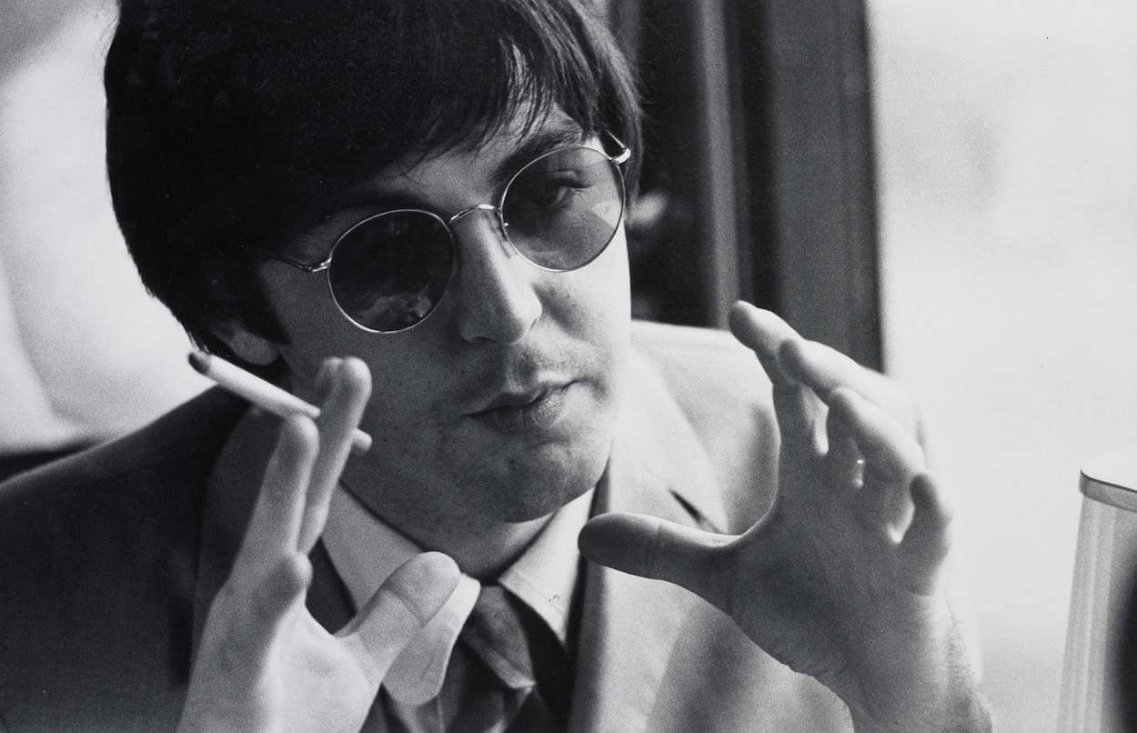 Paul McCartney wearing sunglasses and a suit while holding a cigarette in his right hand in 1966.