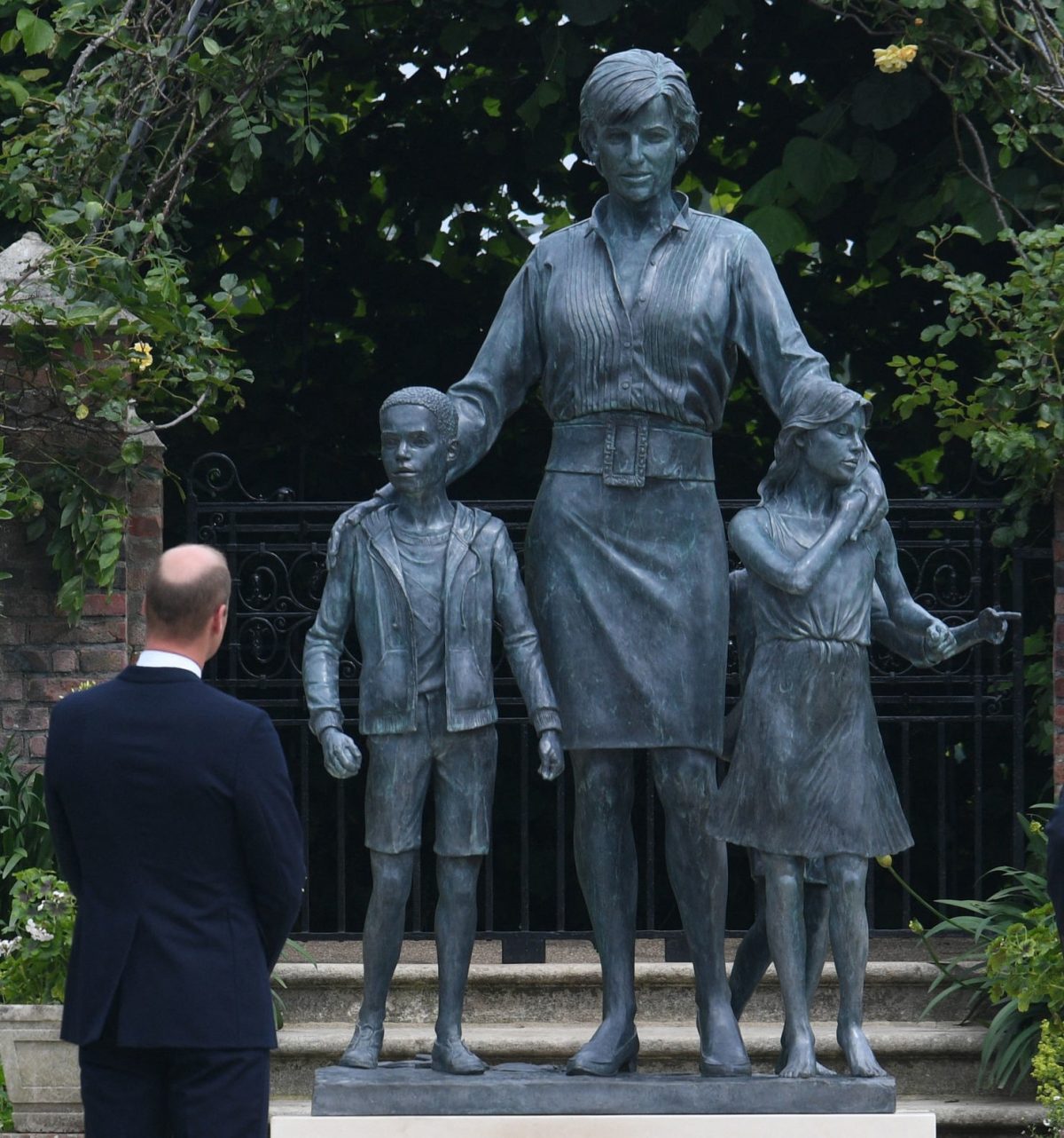 Prince William standing in front of a statue of his mother, Princess Diana, at The Sunken Garden in Kensington Palace