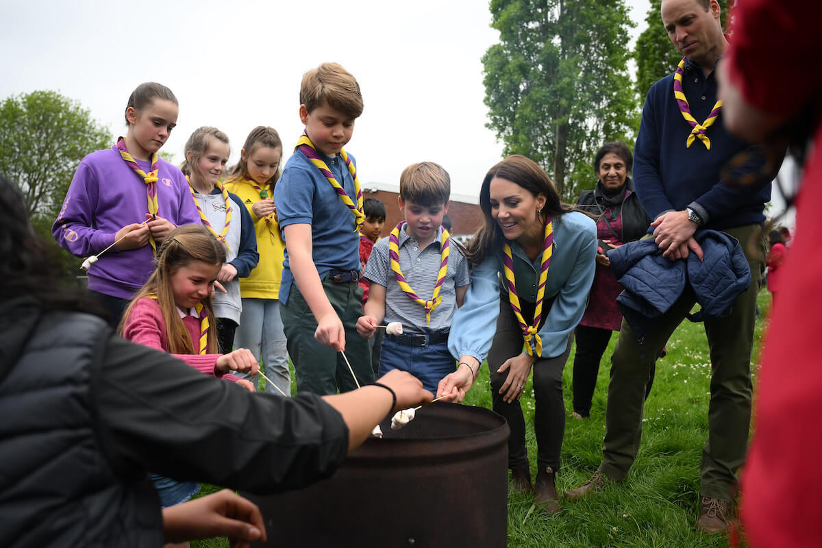 Princess Charlotte, Prince George, and Prince Louis, who 'definitely have chores' and keep track of them via a 'fun chart' made by Kate Middleton, stand with Kate Middleton and Prince William roasting marshmallows