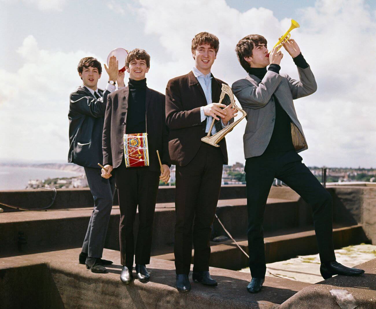 Paul McCartney, Ringo Starr, John Lennon, and George Harrison of The Beatles play small instruments on a rooftop