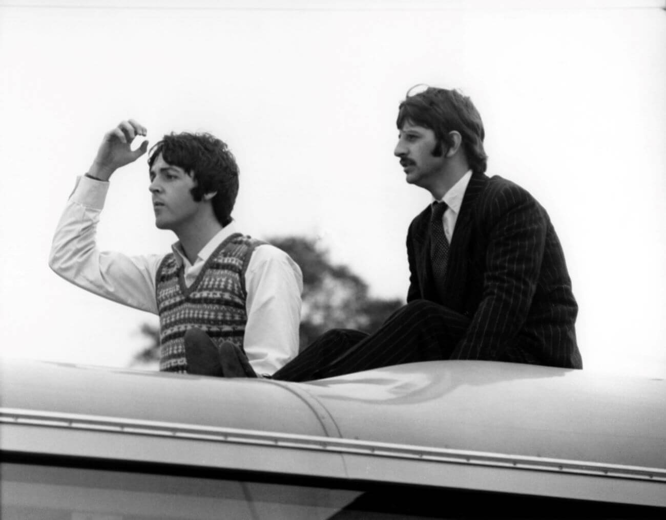 A black and white picture of Paul McCartney and Ringo Starr sitting on top of a bus.