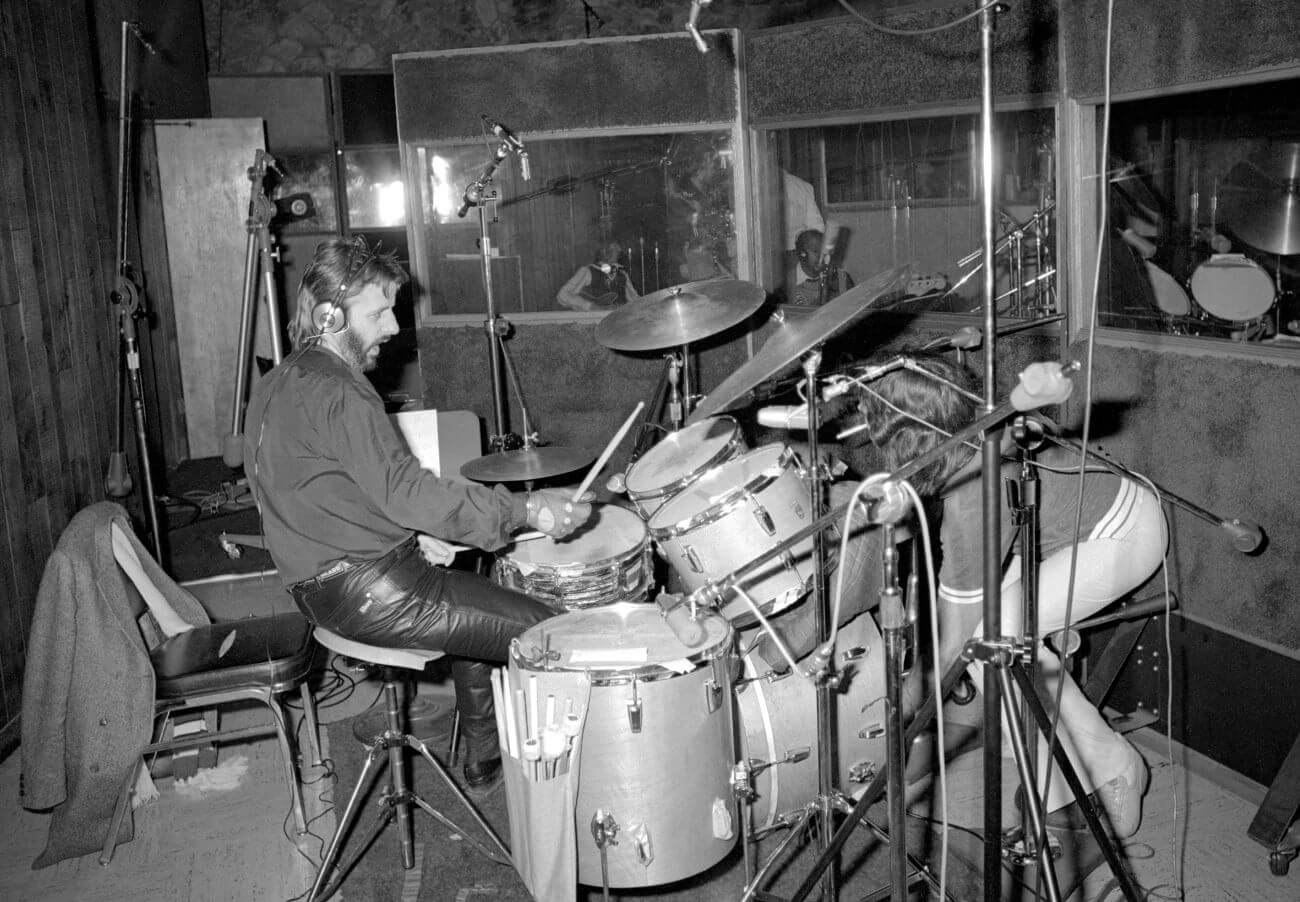 A black and white picture of Ringo Starr wearing headphones and sitting at a drum set.