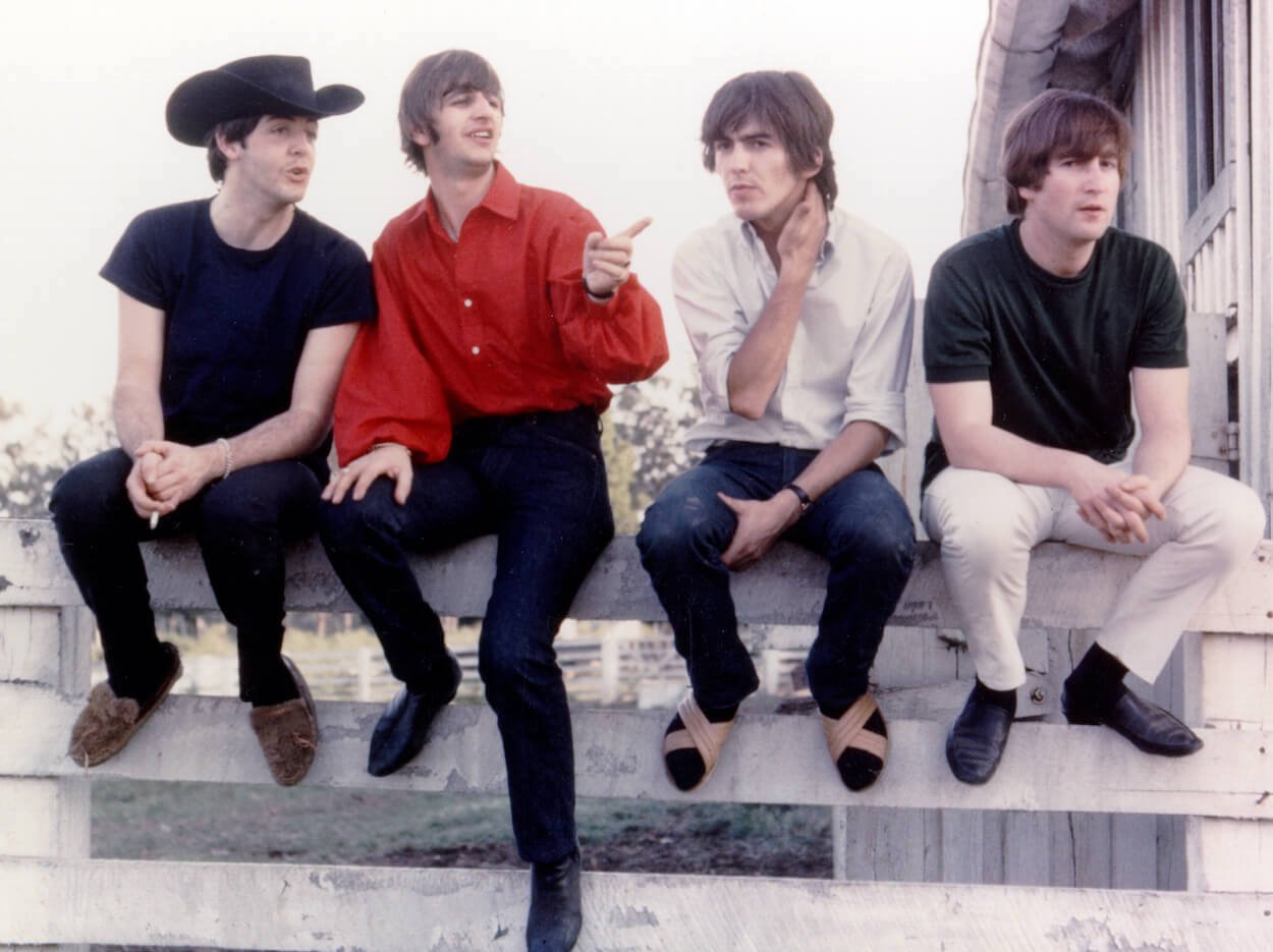 Beatles members (from left) Paul McCartney, Ringo Starr, George Harrison, and John Lennon sitting on a white fence on the set of the movie 'Help!' in 1965.