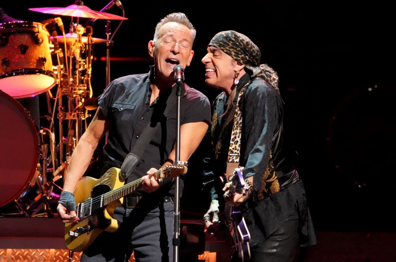 Bruce Springsteen and Steven Van Zandt play guitars and sing into the same microphone.