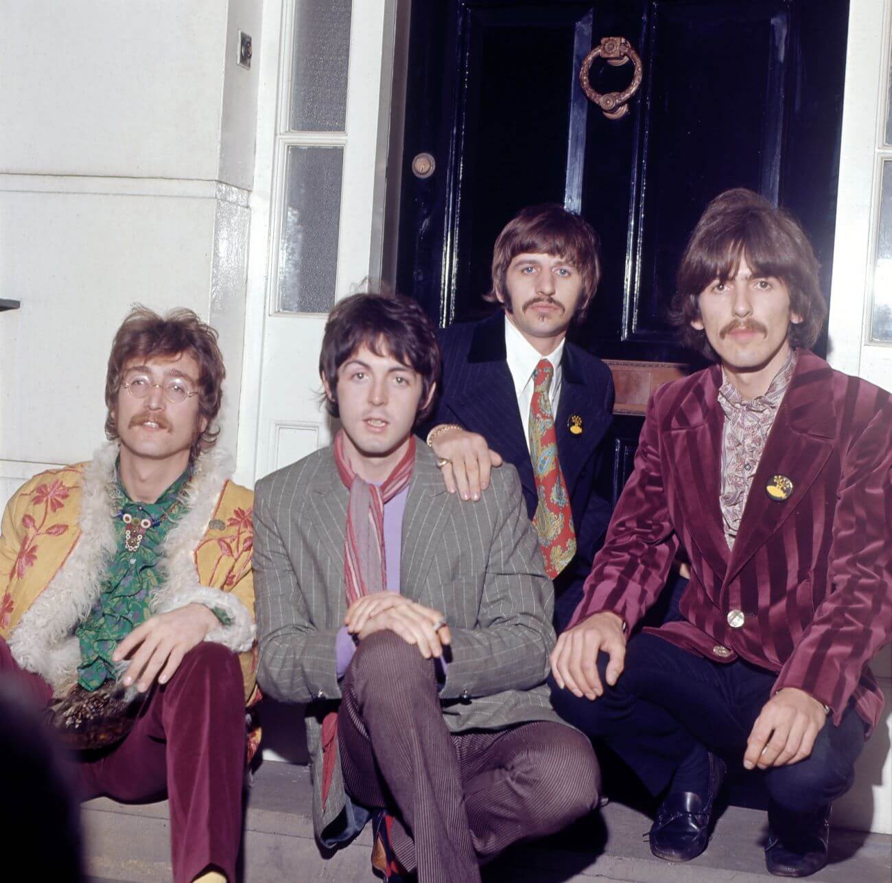 John Lennon, Paul McCartney, Ringo Starr, and George Harrison of The Beatles sit on a doorstep.