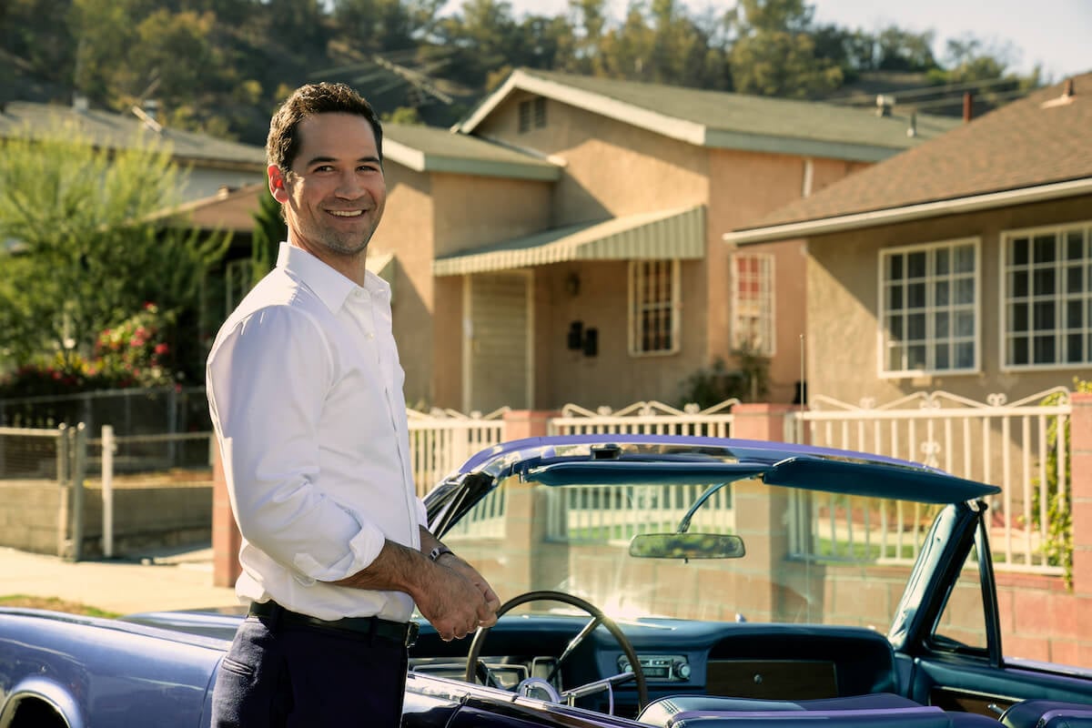 Smiling Manuel Garcia-Rulfo as Mickey Haller standing in front of a house in 'The Lincoln Lawyer' Season 2
