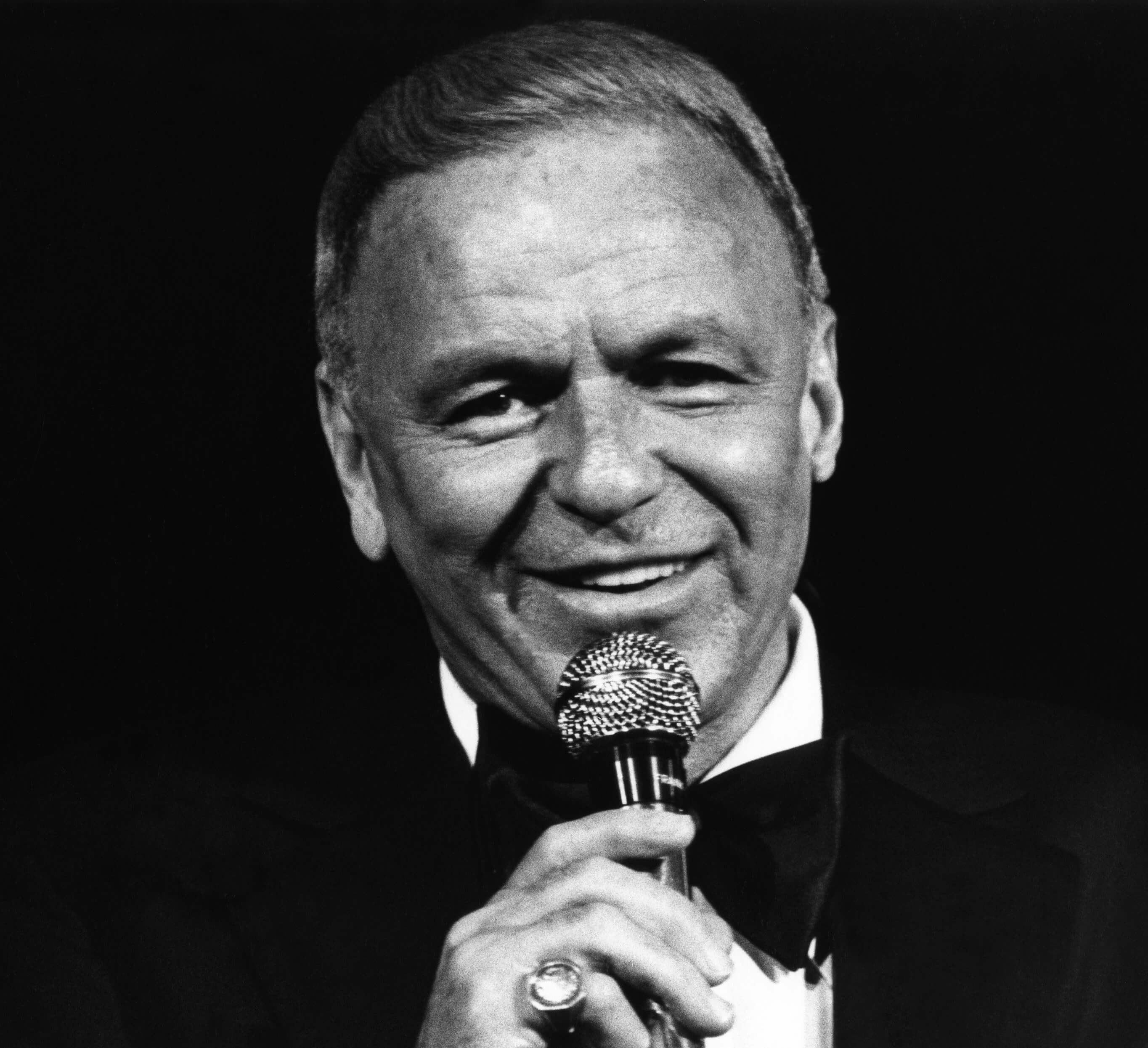 "My Way" singer Frank Sinatra holding a microphone in black-and-white