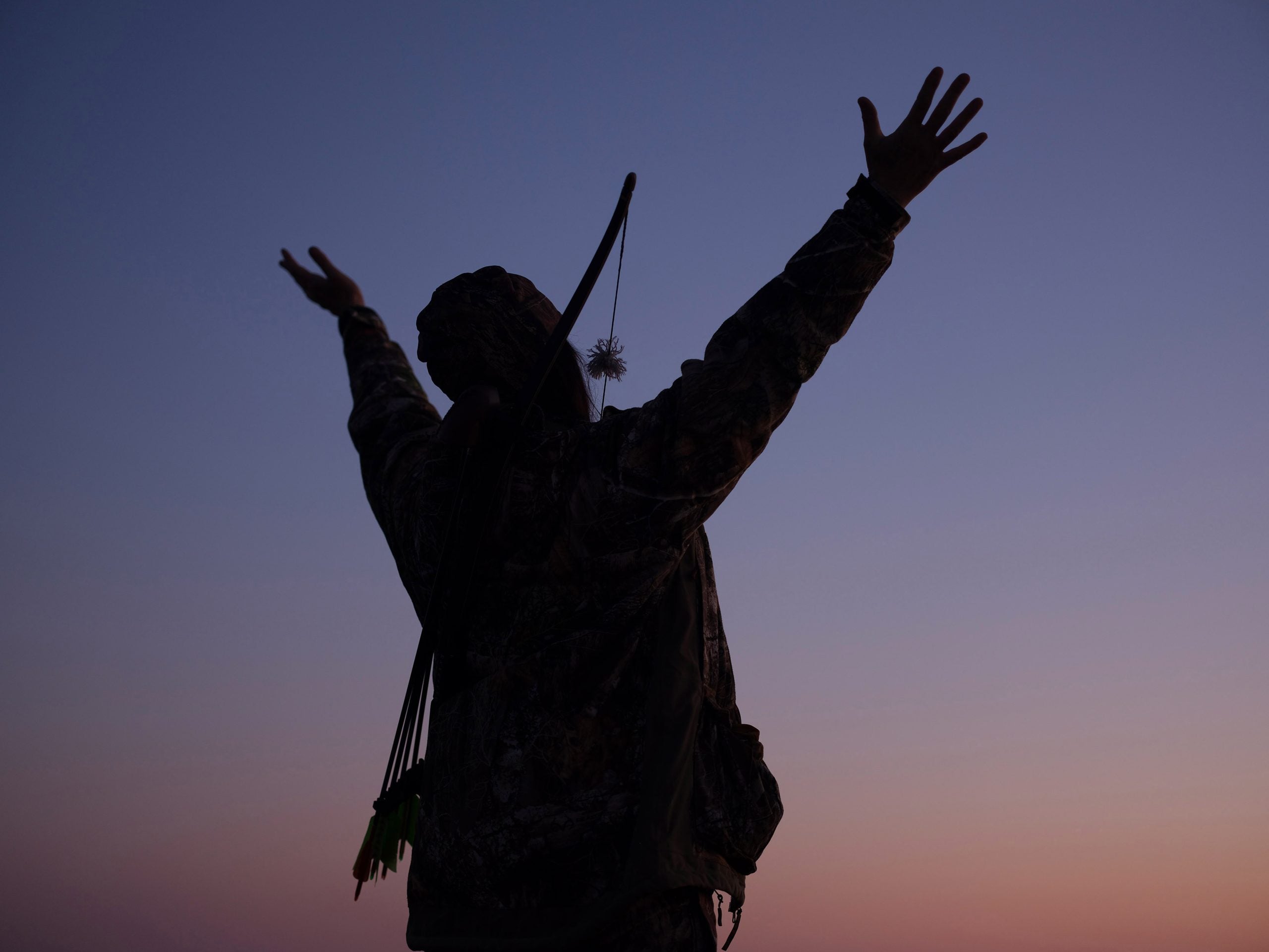 A silhouetted person raising their arms against a blue and orange sky