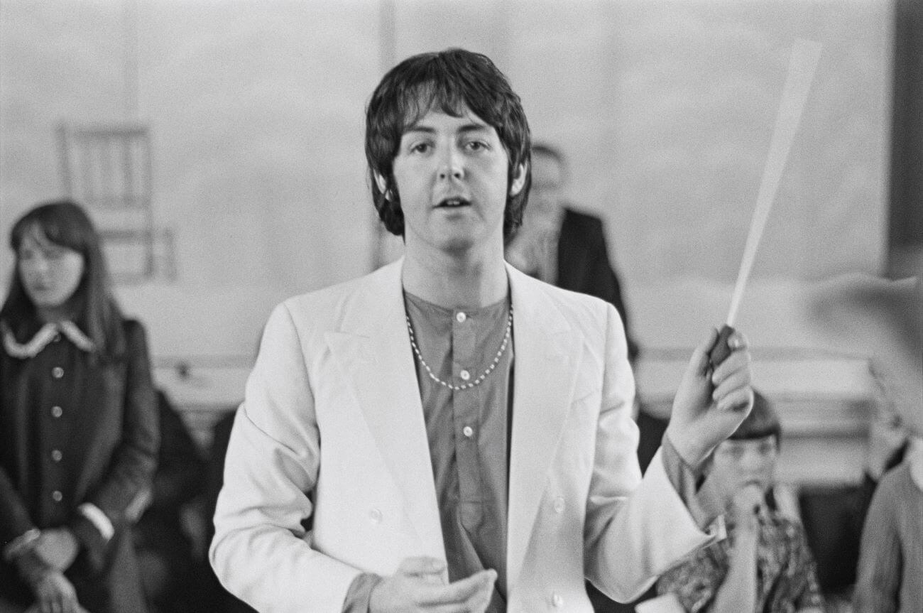 A black and white picture of Paul McCartney wearing a necklace and waving a baton.