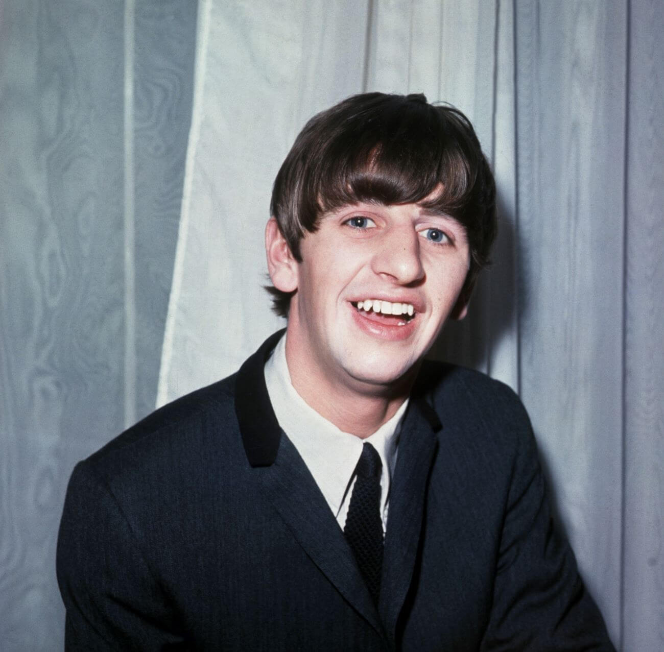 Ringo Starr wears a suit and poses in front of a curtain.