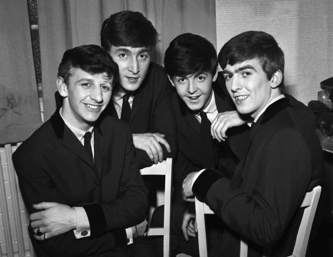 Ringo Starr, John Lennon, Paul McCartney, and George Harrison of The Beatles gather around each other while sitting in front of a window.