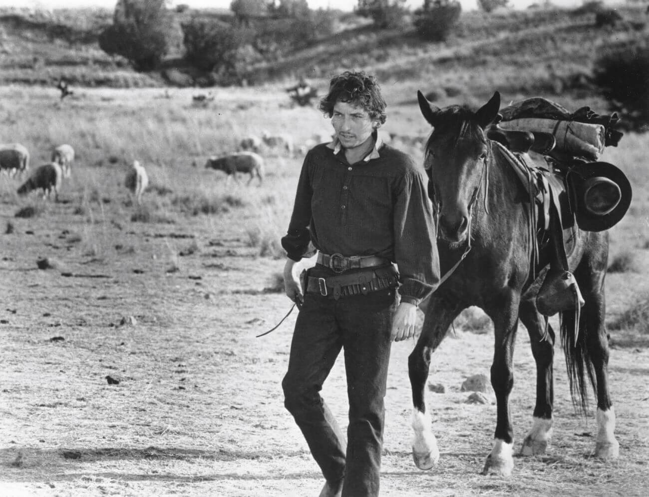 A black and white picture of Bob Dylan walking through the desert with a horse in 'Pat Garrett and Billy the Kid.'