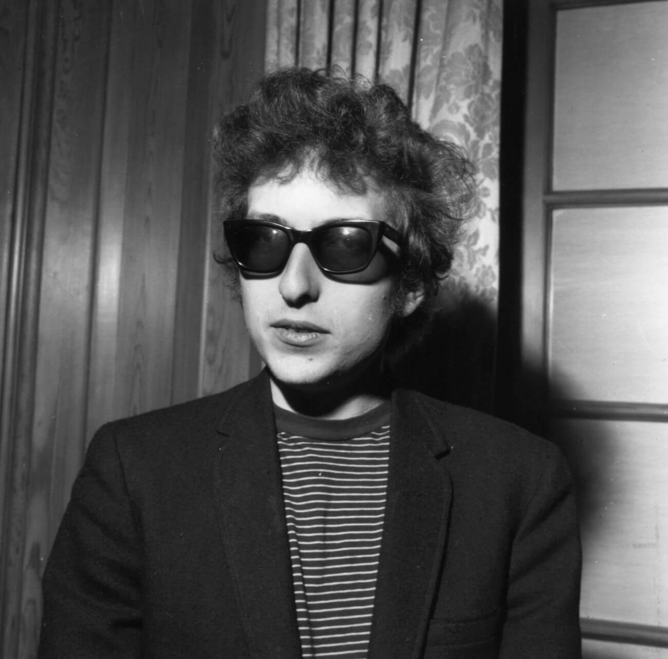A black and white picture of Bob Dylan wearing sunglasses and a striped shirt.