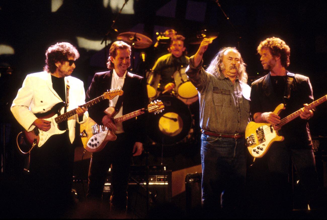 Bob Dylan holds a guitar and stands onstage with Bob Dylan performs with Roger McGuinn, David Crosby and Chris Hillman.