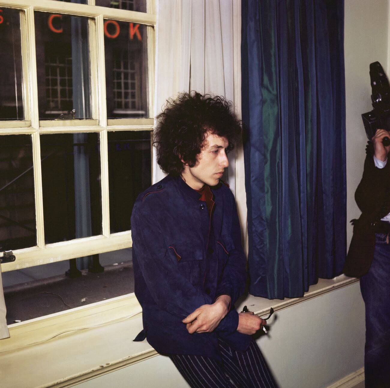 Bob Dylan leans against a window ledge and holds a cigarette.