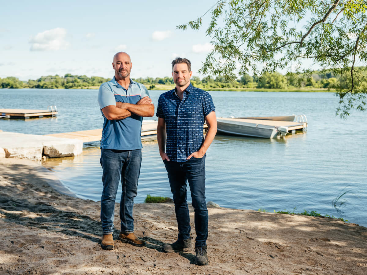 Bryan Baeumler and Scott McGillivray standing on the shores of a lake in a promo shot for 'Renovation Resort Showdown' on HGTV