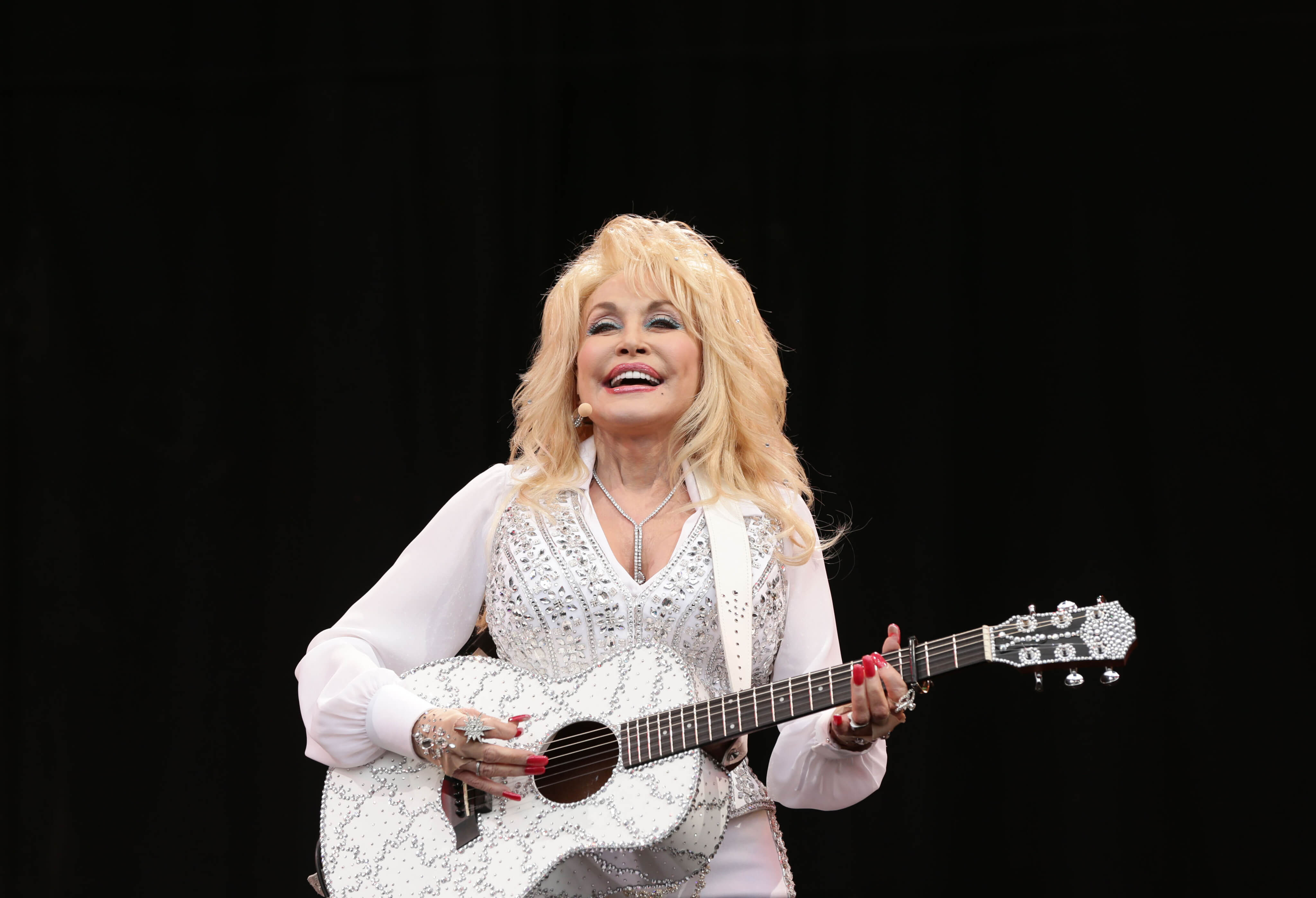 Dolly Parton on stage with a white guitar.