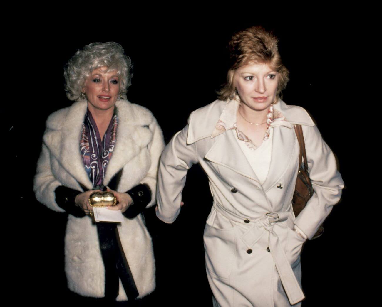 Dolly Parton and Judy Ogle wear coats and walk together. Parton holds a purse and is a step behind Ogle.