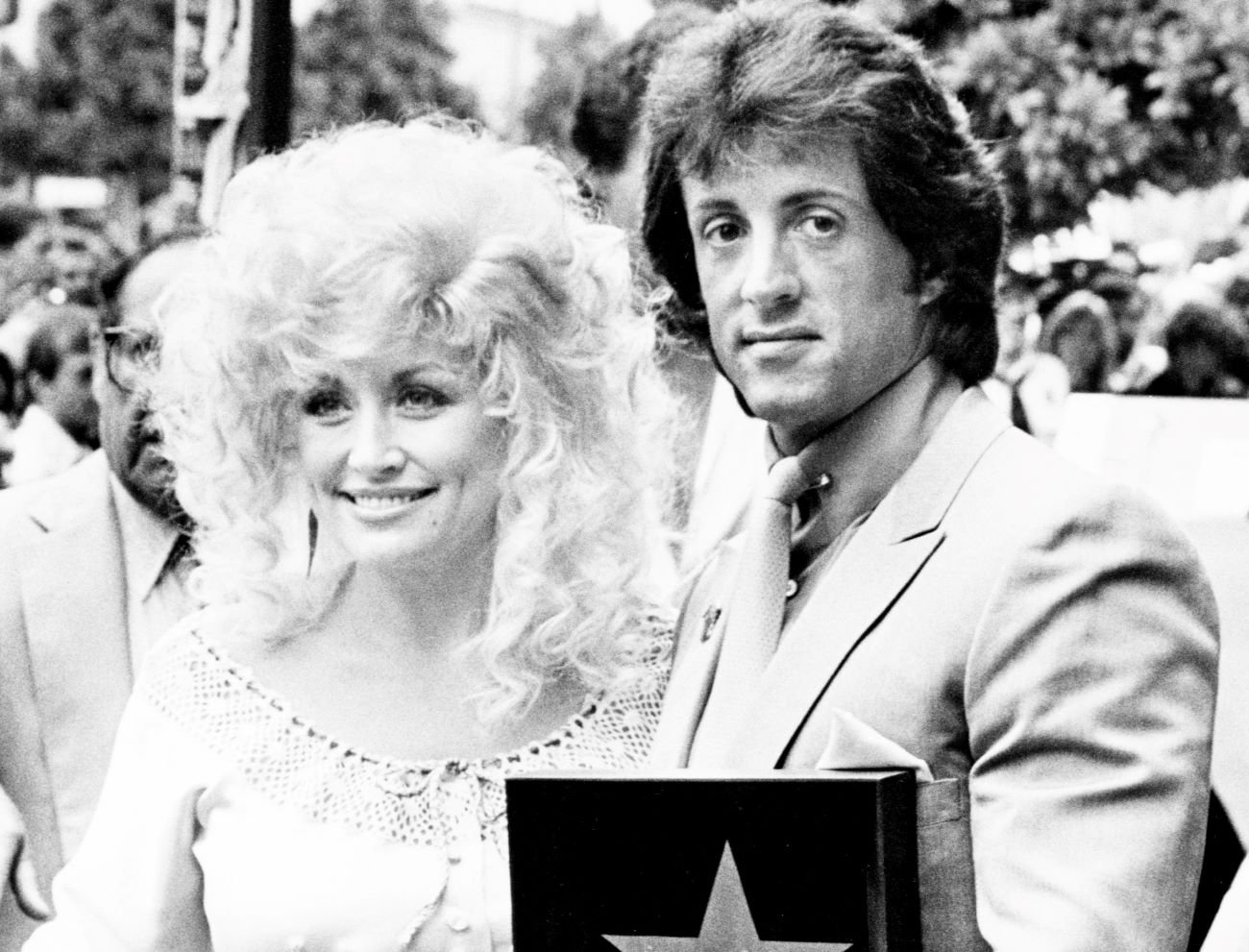 A black and white picture of Dolly Parton and Sylvester Stallone standing together. He holds a plaque with a star on it.