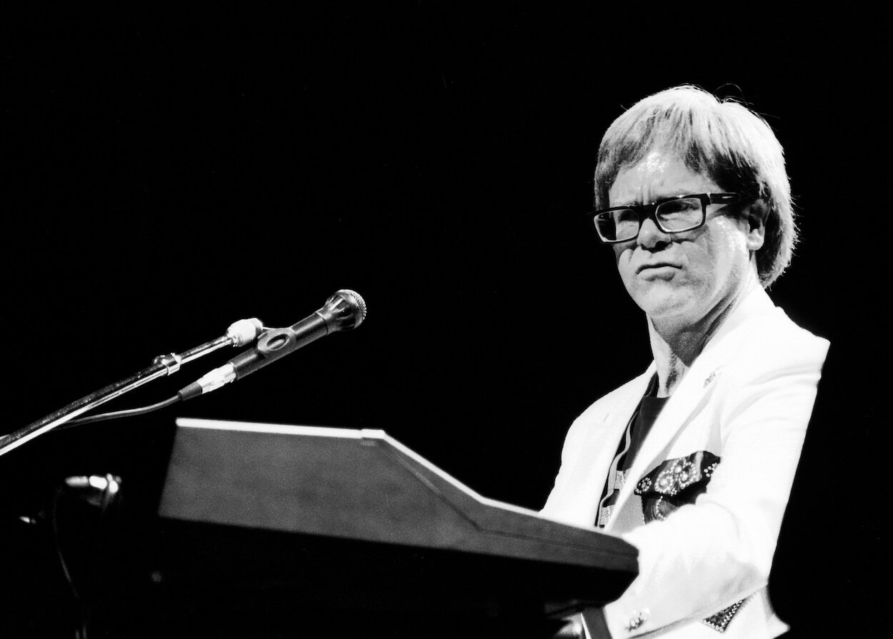 Elton John wearing a white suit and playing piano during a 1992 concert.