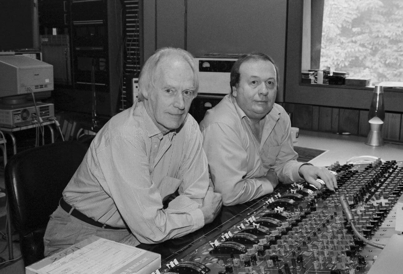 A black and white photo of George Martin and Geoff Emerick sitting at a mixing desk in a studio.