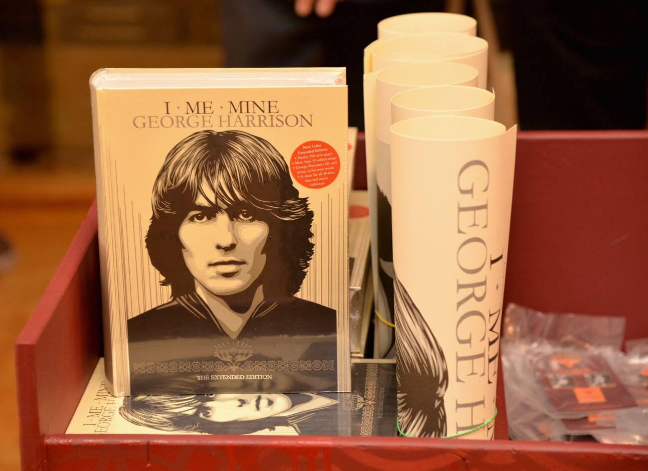 A copy of George Harrison's book "I, Me, Mine," stands up next to five rolled up posters.