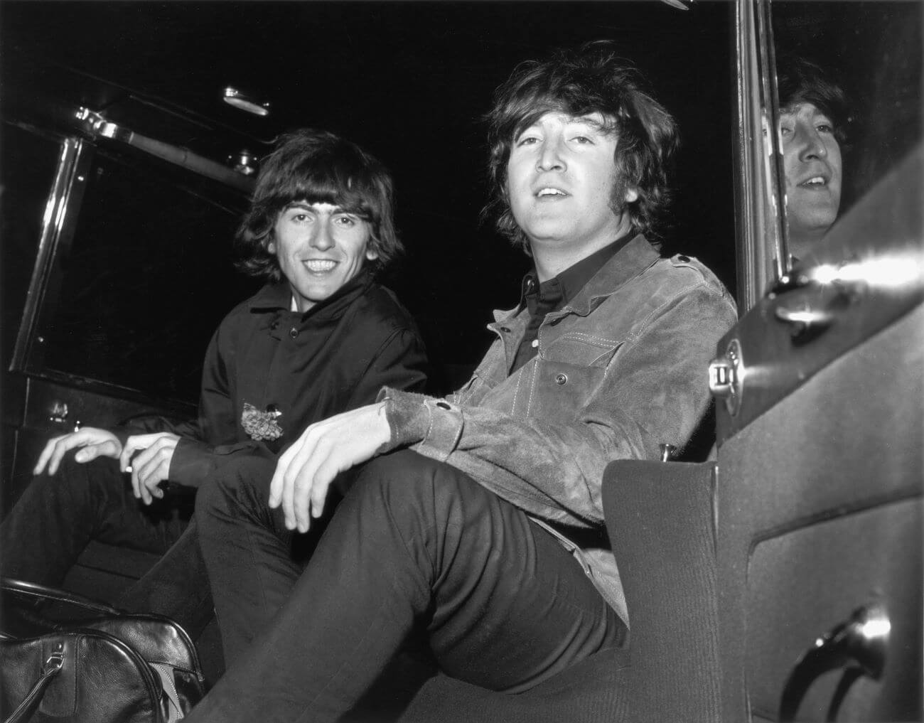 A black and white picture of George Harrison and John Lennon sitting in the back of the car together.