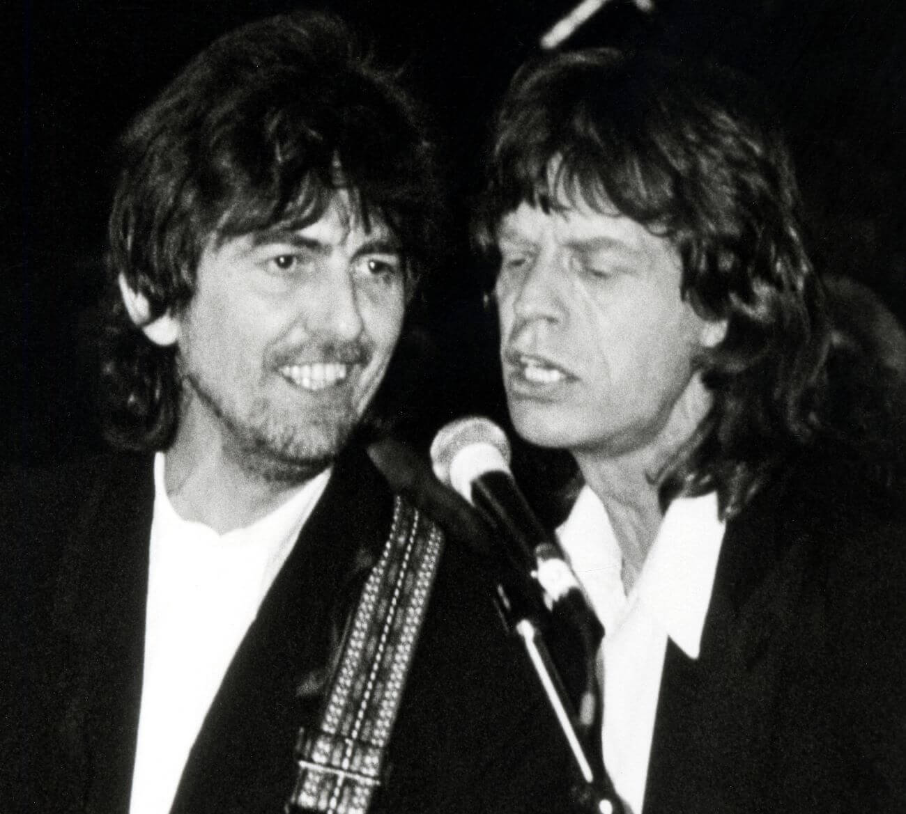 A black and white picture of George Harrison and Mick Jagger singing into the same microphone.