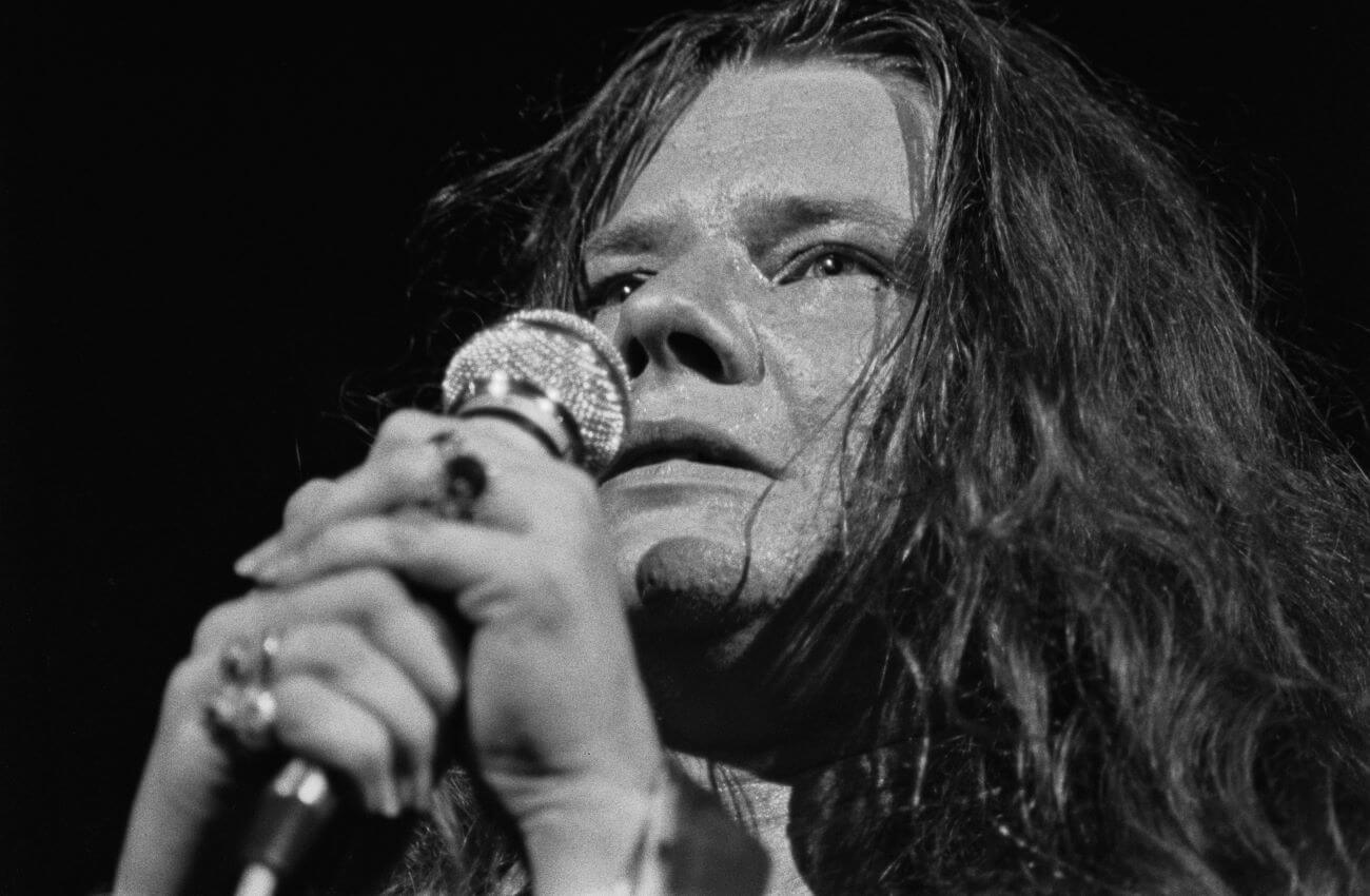 A black and white picture of Janis Joplin holding a microphone up to her face.