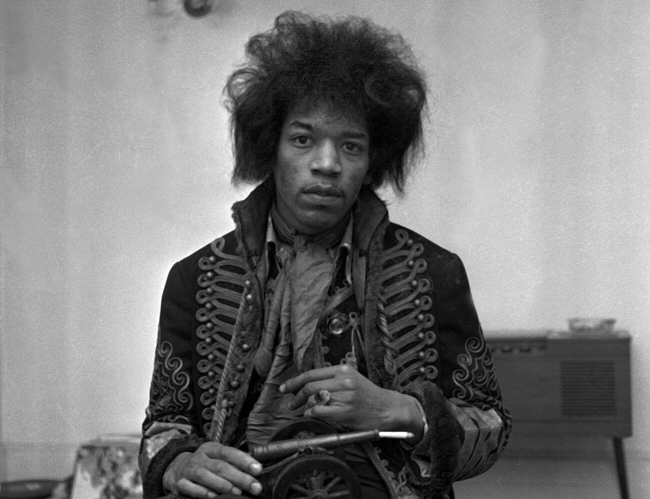 A black and white picture of Jimi Hendrix holding a miniature cannon. 