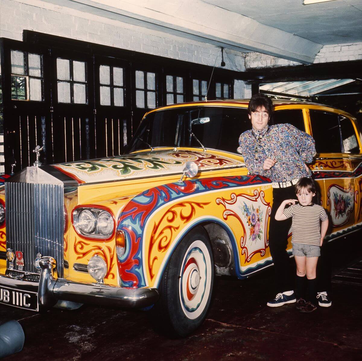 John Lennon leans on his yellow Rolls-Royce while his young son Julian stands in front of him.