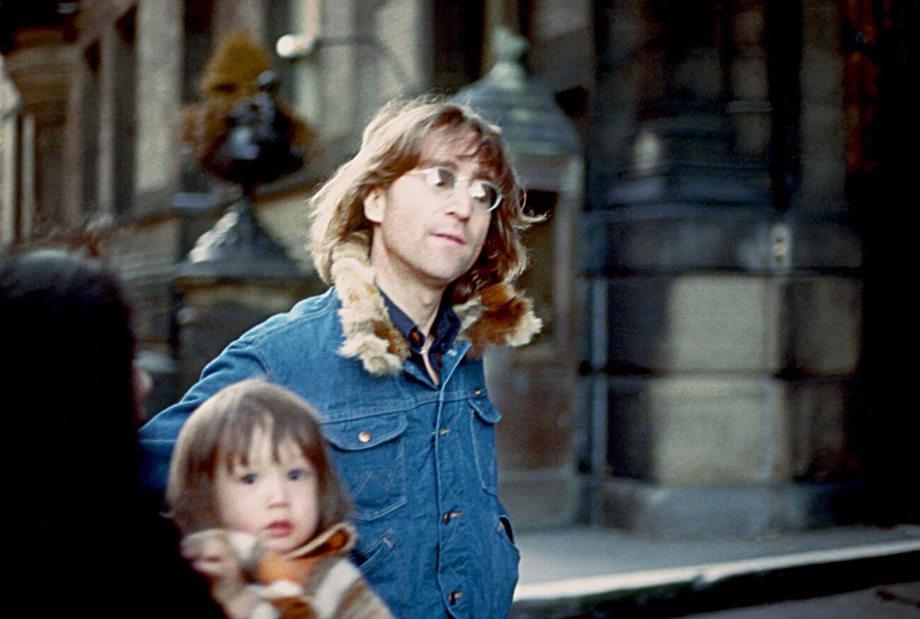 John Lennon wears a denim jacket and stands near his baby son Sean.
