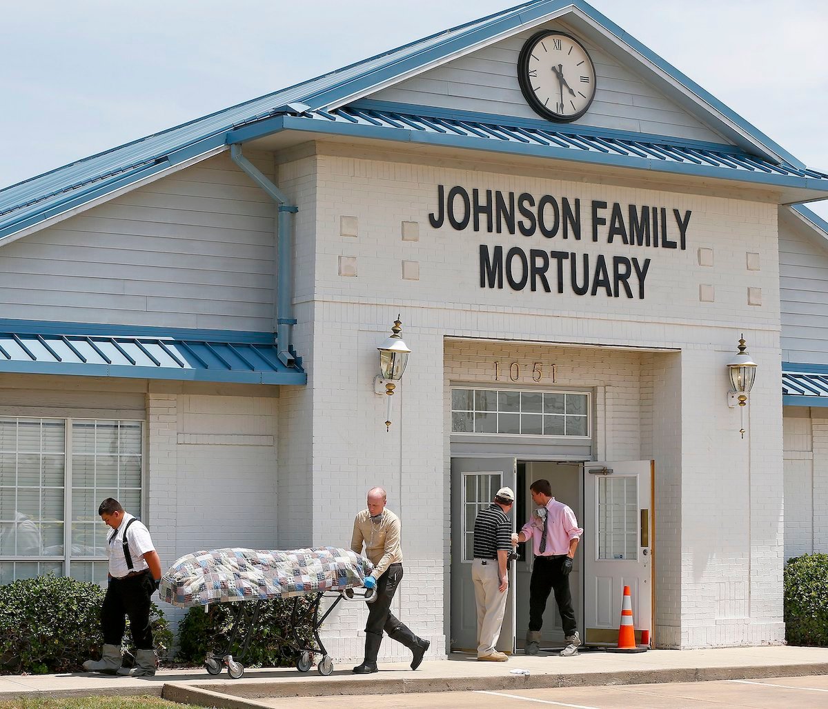 Exterior of the Johnson Family Morturary as people wheel away a covered body on a stretcher