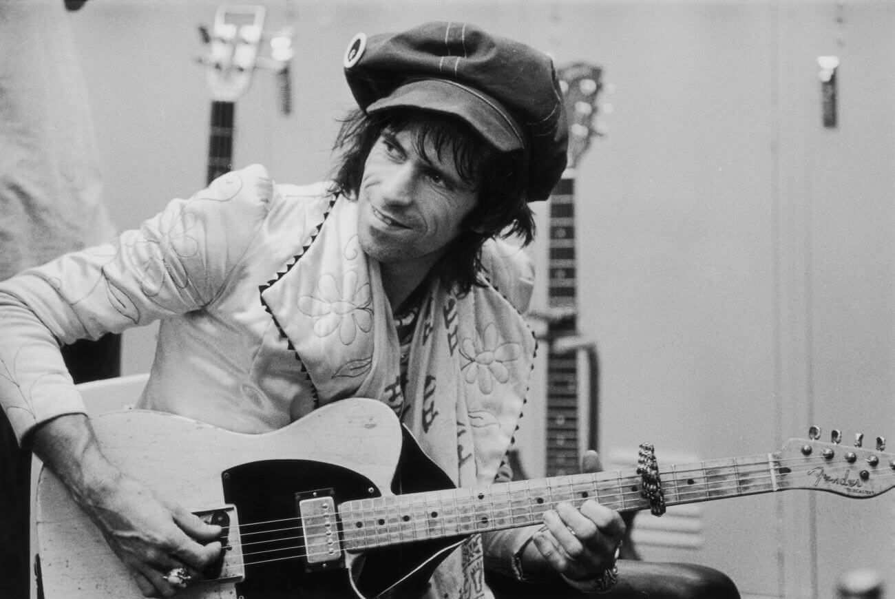 A black and white picture of Keith Richards wearing a hat and playing guitar.