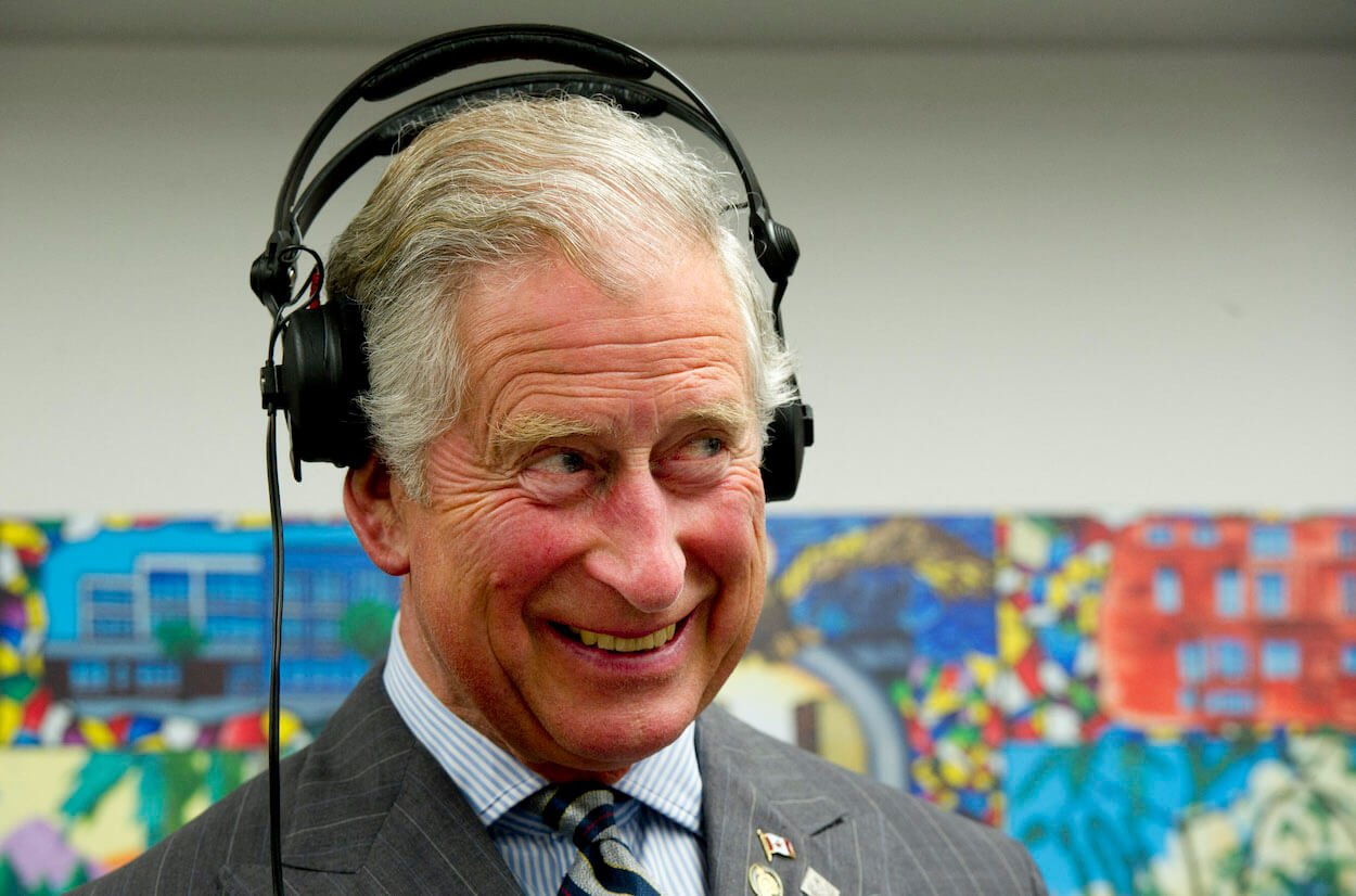 King Charles smiling and wearing headphones during a 2012 visit to Canada.