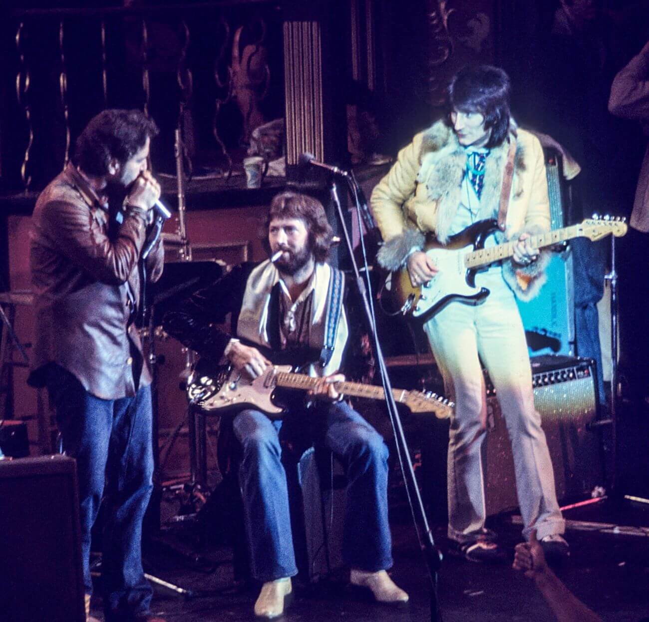 Paul Butterfield holds a microphone next to Eric Clapton and Ronnie Wood, who play guitars.