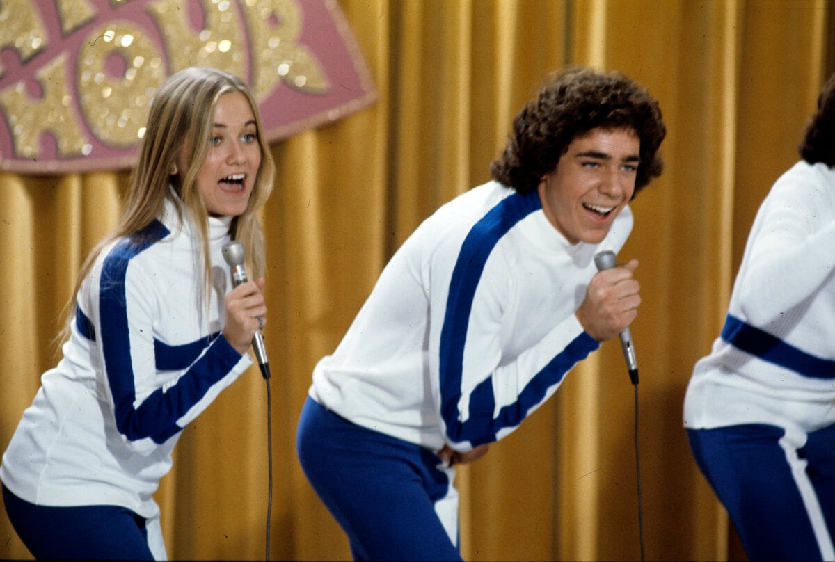 Maureen McCormick and Barry Williams singing into microphones in an episode of 'The Brady Bunch'